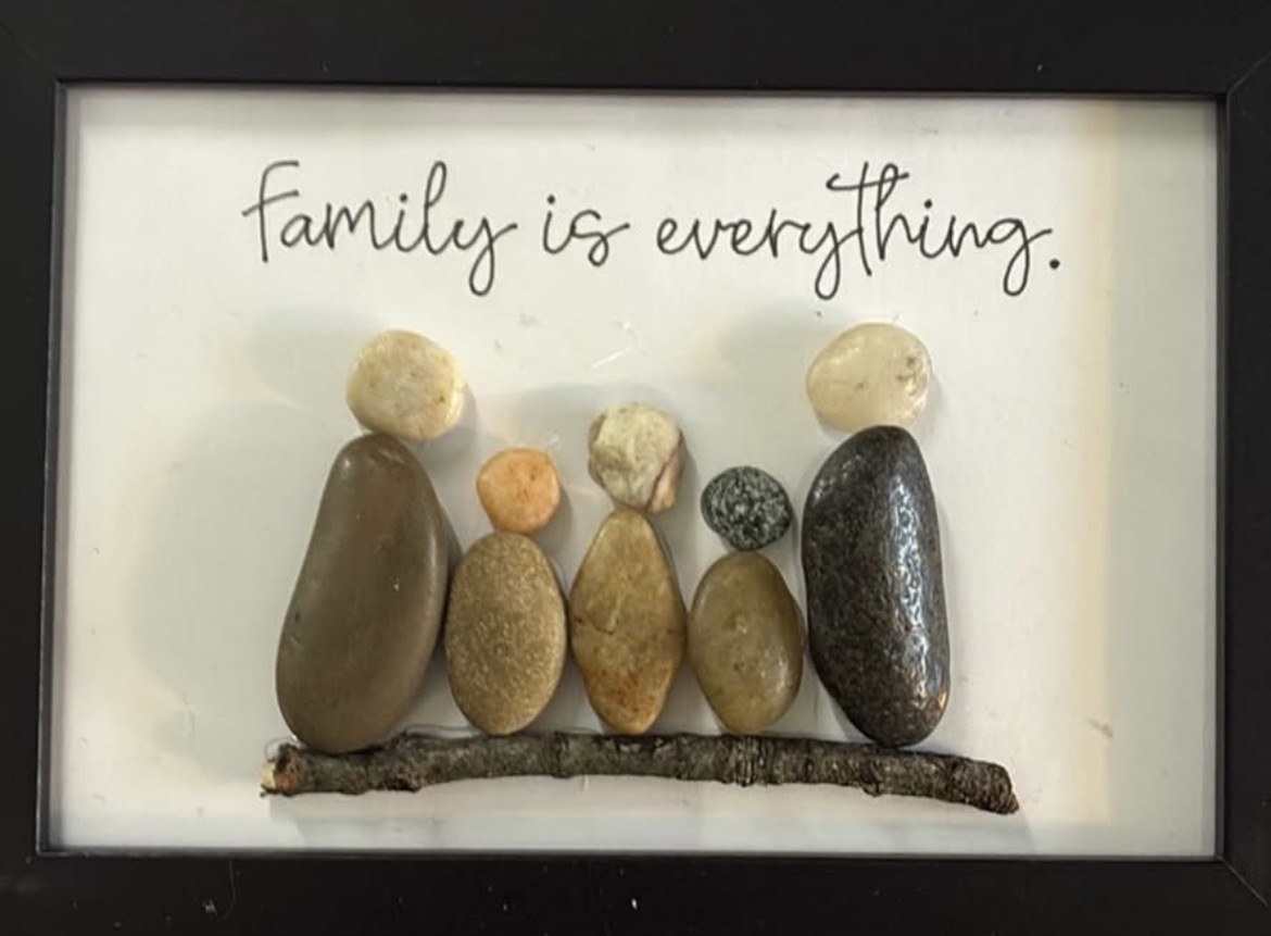 Five pebble people arranged on a twig in a black frame with the words Family is everything