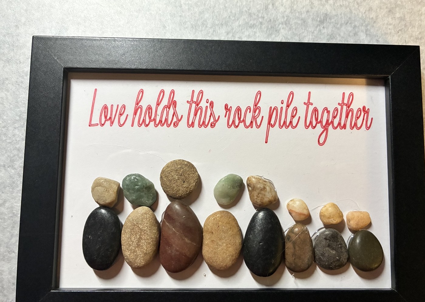 Eight pebble people in a black frame with Love holds this rock pile together written in red