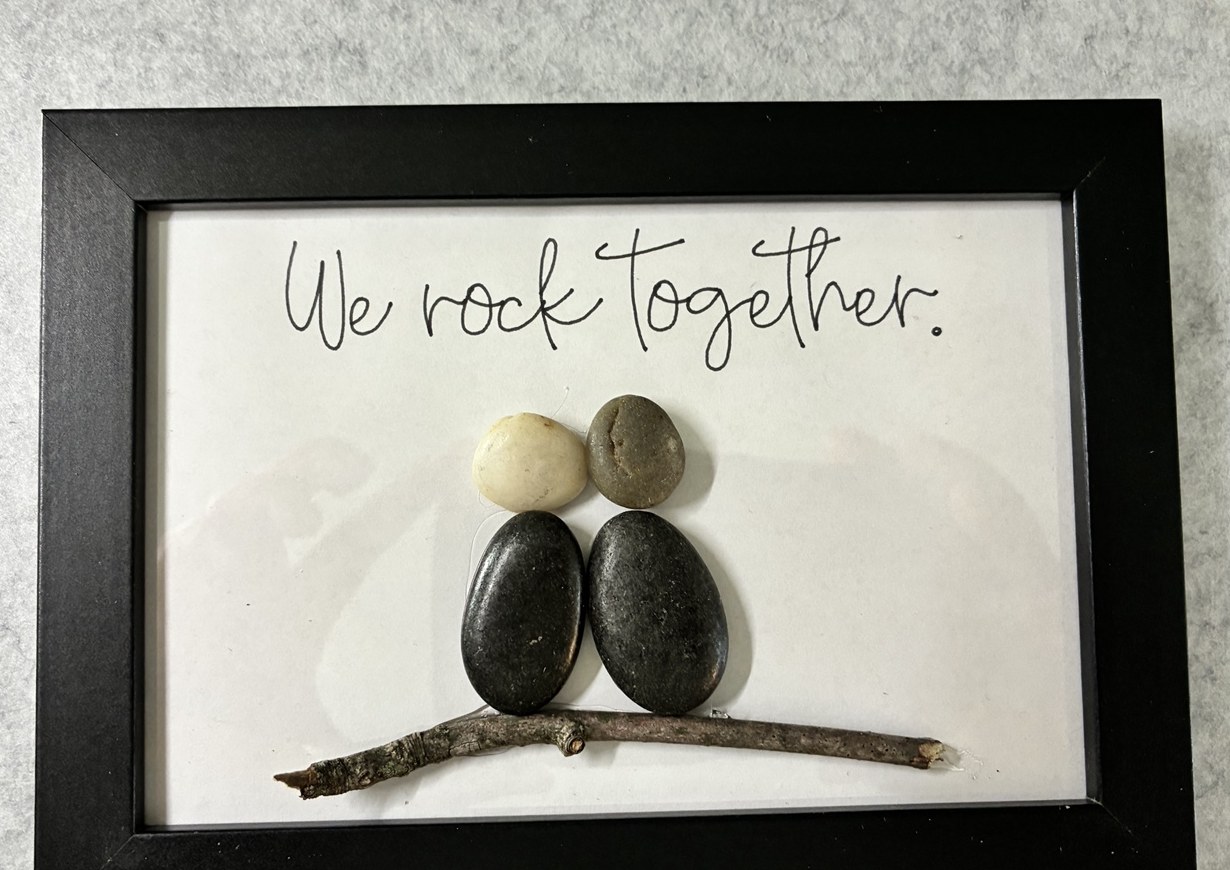 Two dark pebble people side by side beneath the handwritten phrase We rock together